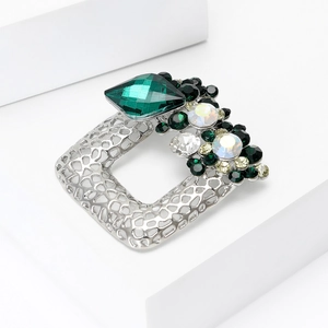 Detailed view of a silver-tone geometric brooch featuring green crystals and rhinestones