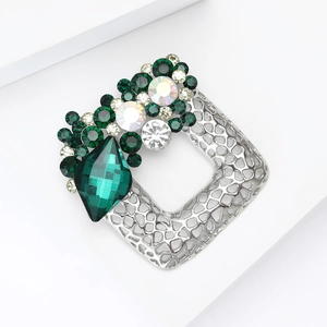Detailed macro of a silver alloy square brooch featuring green crystals and emerald gemstone