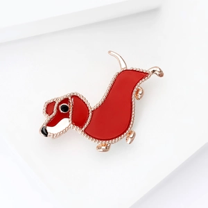 Polished red enamel dachshund brooch with gold metal trim on a white display stand