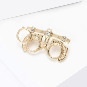 Creative gold optometrist frame brooch with sparkling white rhinestones on a white stand