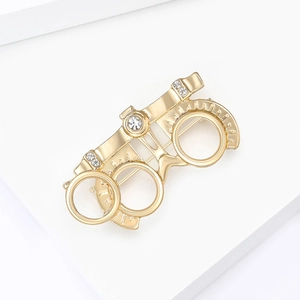 Detailed close-up of golden optometry frame brooch with rhinestones on white blocks