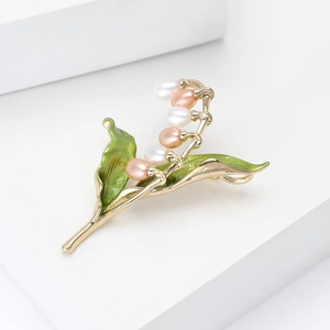 Détail d'une broche muguet avec perles et émail vert sur une base dorée élégante
