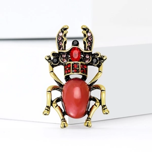 Vintage Käfer Brosche in Gold mit rotem Stein und bunten Strasssteinen auf weißem Tisch