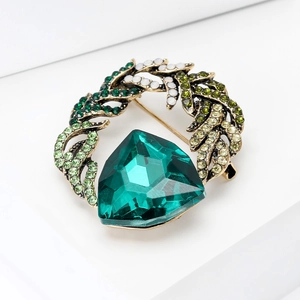 Macro shot of emerald green crystal brooch with vintage gold leaf setting on white background