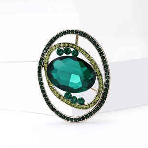 Vintage green crystal planet brooch with layered rhinestone borders on a white pedestal