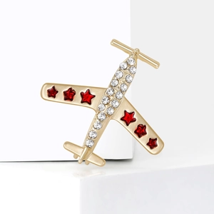 Broche avion dorée avec strass blancs et étoiles rouges sur un support en pierre blanche