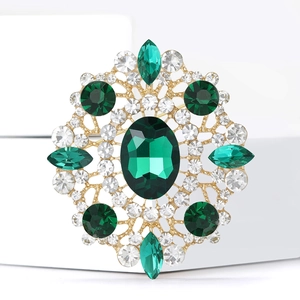 Macro shot of large oval emerald rhinestone brooch with golden filigree and crystals