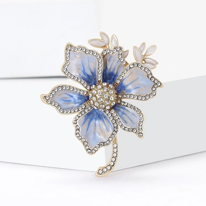 Elegant gold flower brooch with blue enamel petals and sparkling white rhinestones on white