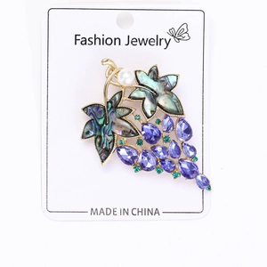 Detail view of grape brooch with purple crystals and abalone shell on display card