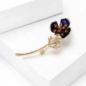 Close-up of blue enamel poppy flower brooch with golden stem on a white platform