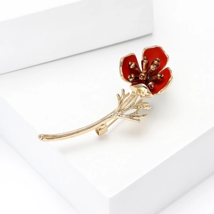 Close-up of red enamel poppy brooch with gold metal stem on white geometric props