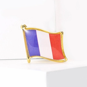 Macro shot of French flag enamel brooch with gold-tone metal border on a white pedestal