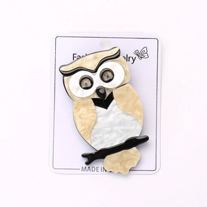 Détail macro d'une broche hibou en acrylique avec texture marbrée nacrée et design rétro