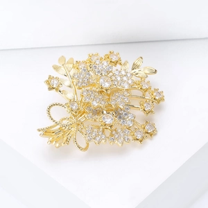 Detailed close-up of a zircon bouquet brooch with a golden bow on a white pedestal