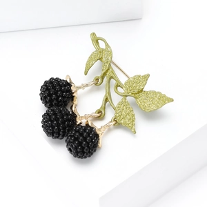 Detail of enamel blackberry brooch with black berry clusters and green leaves on a white block