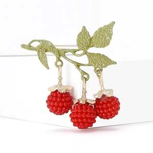 Elegant gold enamel berry brooch with green leaves and red raspberries on a white stand