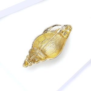 Detail of golden seashell brooch back showing the metal safety pin and textured surface