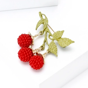 Macro detail of enamel blackberry brooch with red berries and green leaves on gold metal
