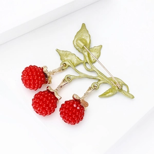 Macro view of a gold-tone berry brooch with red raspberry texture and green enamel leaves