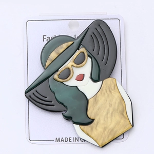 Détail d'une broche moderne en acrylique représentant une femme avec chapeau et robe jaune