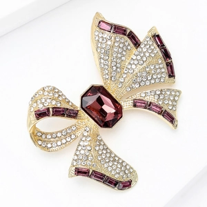 Close-up of luxury gold bow brooch with sparkling white diamonds and purple gemstones