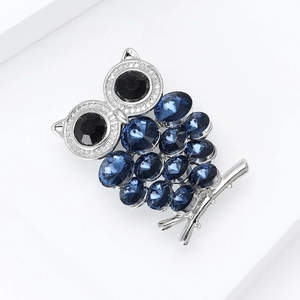 Detailopname van een zilveren uil-broche met blauwe kristallen en zwarte stenen