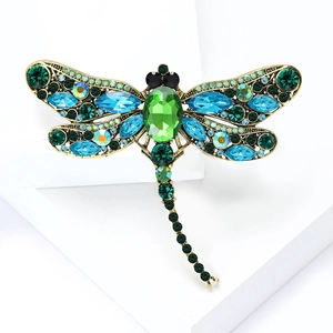 Vintage gold dragonfly brooch with vibrant green and blue rhinestones on white display