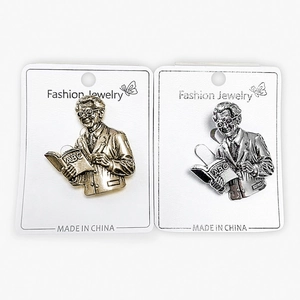 Macro shot of vintage metal brooch featuring a detailed old man figure holding an ABC book