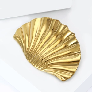 Elegant gold shell jewelry tray with radial texture on a minimalist white display pedestal