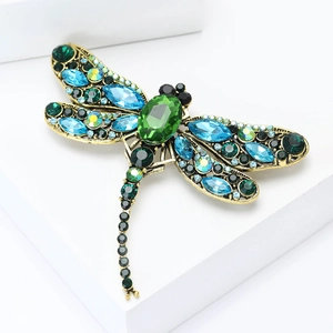 Exquisite gold-plated dragonfly brooch with green and blue rhinestones on white pedestal