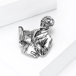 Detailed close-up of a vintage silver brooch shaped like a teacher holding an ABC book