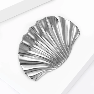 Close-up of a silver polished shell-shaped brooch with textured radial ridges and waves