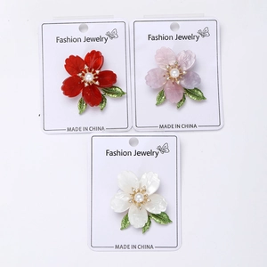 Detailed macro view of three enamel flower brooches in red, purple, and white variants