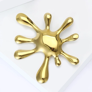 Macro view of gold stainless steel splash-shaped brooch with a polished mirror finish