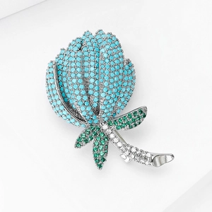 Vue macro d'une broche tulipe sertie de gemmes bleues et vertes sur des socles blancs