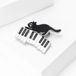 Broche chat noir artistique sur touches de piano avec yeux en pierres précieuses vertes