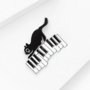 Détail d'une broche en émail chat noir sur un clavier de piano avec yeux en pierre verte