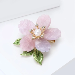 Detailed shot of enamel flower brooch with pink petals, white pearl and golden leaves