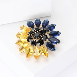 Détail de la broche tournesol en strass bleus et jaunes sur un support géométrique blanc