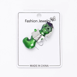 Detailed view of an enamel green bookworm brooch with mortarboard on a white card
