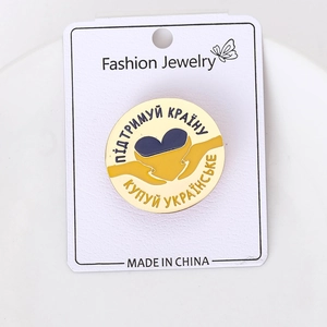 Detailed close-up of a blue and yellow peace dove enamel pin on a white jewelry card