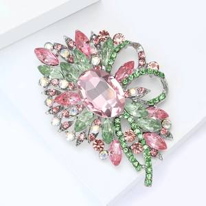 Détail macro d'une broche florale argentée avec cristaux roses et verts sur bloc blanc