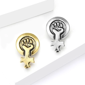 Broches vintage médaille poing féministe en or et argent sur socles blancs