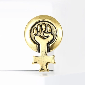Détail d'une broche féministe vintage dorée avec symbole de poing sur socle blanc