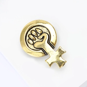 Détail d'une broche féministe vintage dorée avec poing et finition métallique texturée