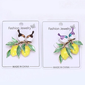 Détail de deux broches en émail avec des citrons jaunes et des oiseaux sur épingle