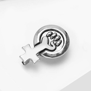Vue macro d'un badge féministe argenté montrant le symbole de Vénus avec un poing