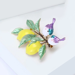 Détail d'une broche citron en émail avec oiseaux sur branche en alliage doré sur fond blanc