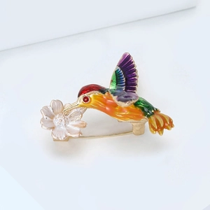 Détail d'une broche colibri en émail coloré avec des détails floraux métalliques