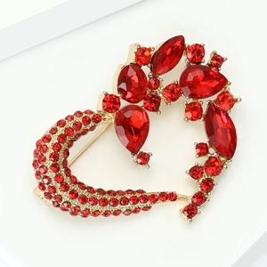 Close-up of heart-shaped gold brooch featuring faceted red rhinestones and teardrop crystals